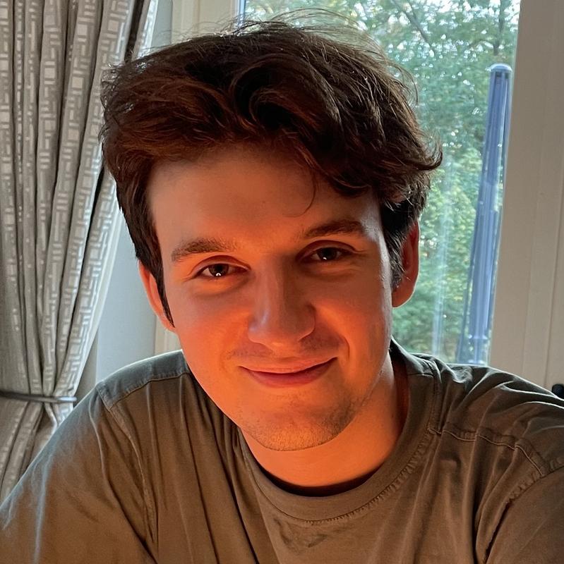 Jack wearing a blue jumper and black headphones, peering over his laptop at the camera